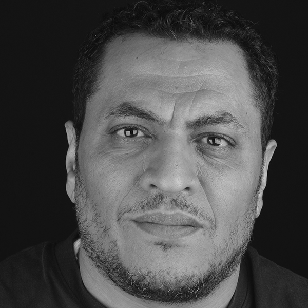 ortrait of a middle-aged man with a serious expression, wearing a dark shirt, captured in black and white against a neutral background